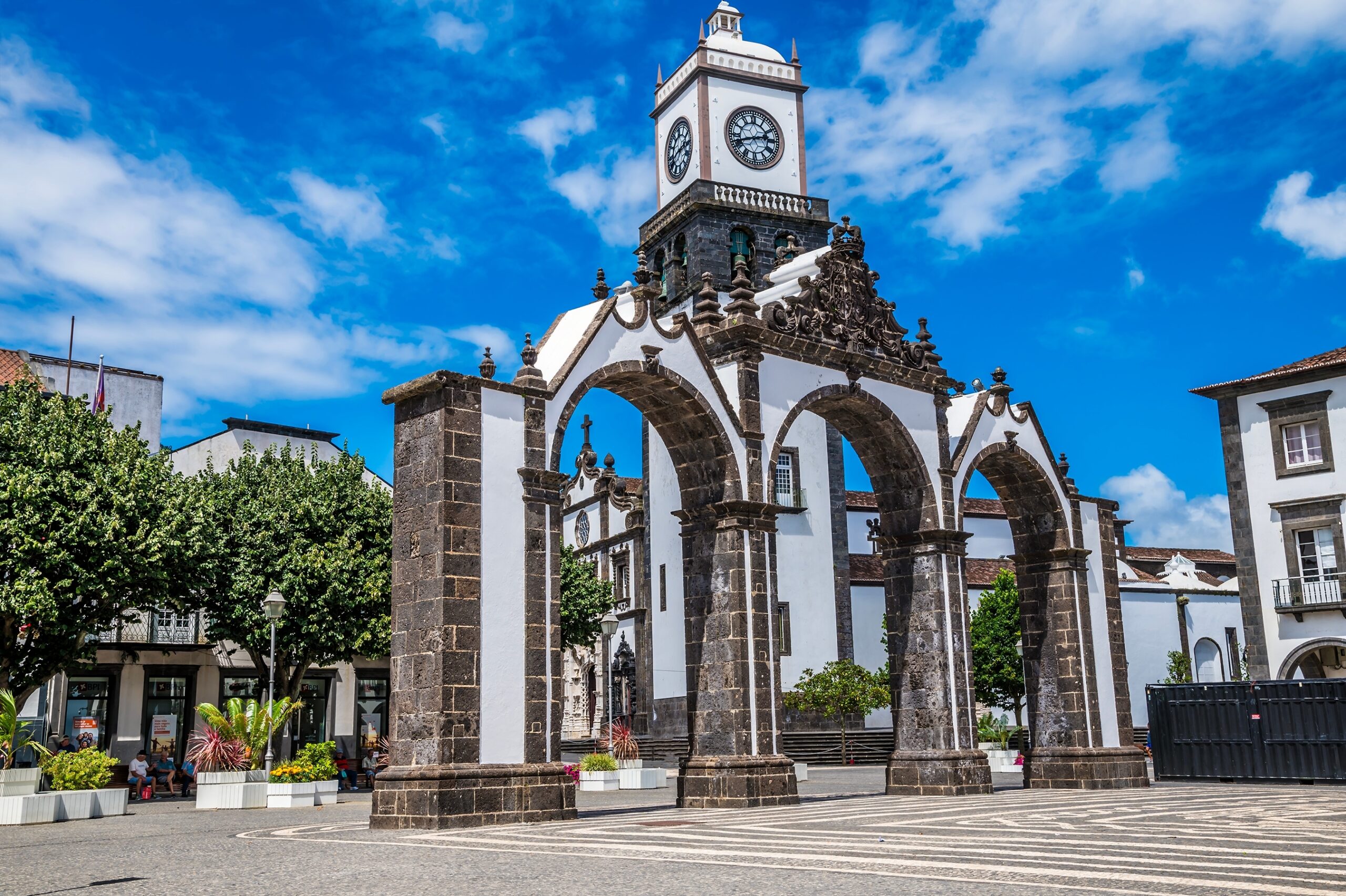 Historic archway with clock tower, surrounded by trees and buildings under a blue sky, showcasing the charm of the town square.