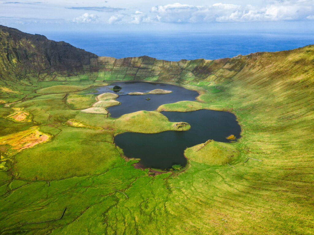 Aerial view of a lush volcanic crater with green slopes and multiple small lakes, showcasing the natural beauty of the landscape.