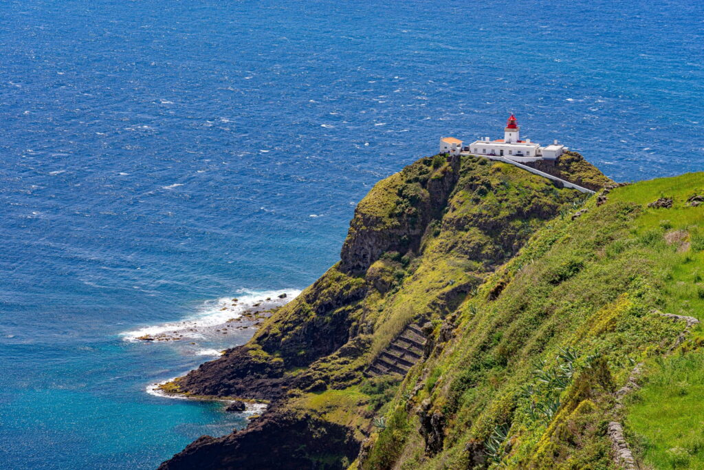 Lighthouse on a rugged cliff overlooking the ocean, surrounded by lush greenery and blue waters. Highlights maritime navigation and scenic beauty.